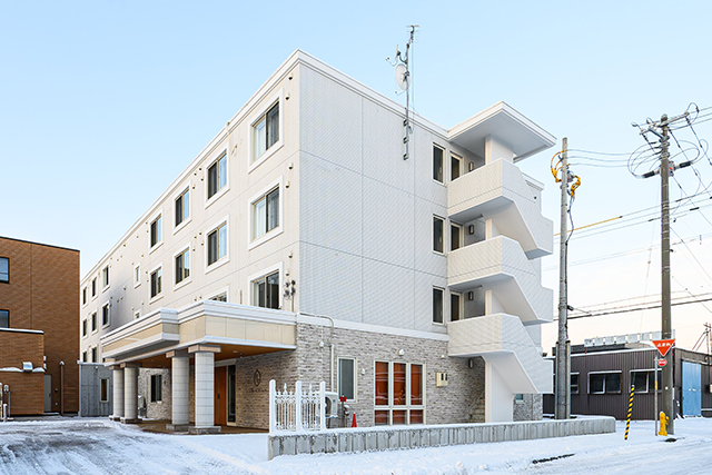 白を基調とした4階建ての介護施設の外観。冬季で雪が積もった周辺環境。
