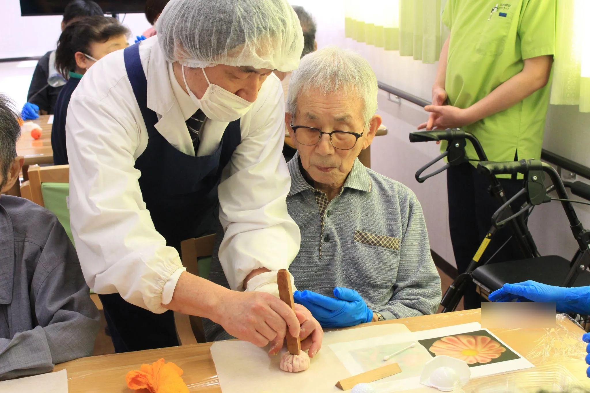 桔梗屋織居の中村様が、ご入居者さまの作った桃色の菊の練り切りに、へらで花芯を付けている。ご入居者さまがその手元を見つめている